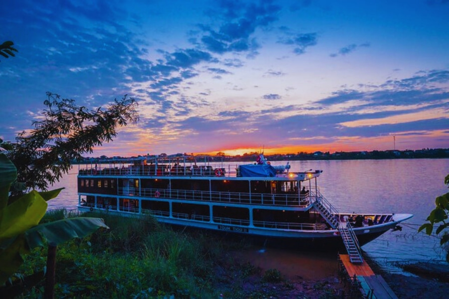 Mekong River Cruise docked at sunset with vibrant sky and calm waters by Auasia Travel
